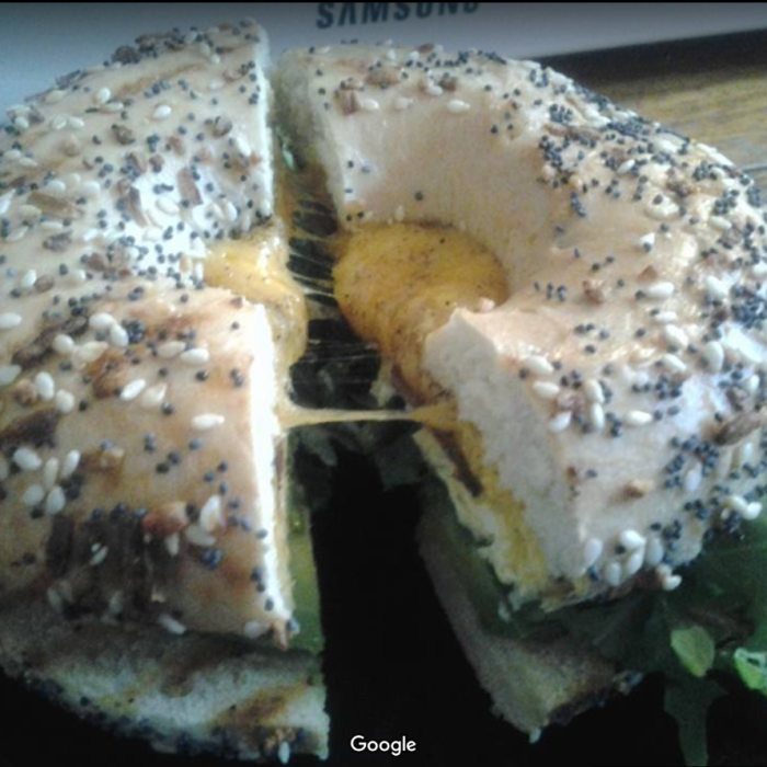 A bagel sandwich being pulled apart, with melted cheese strung between the halves.